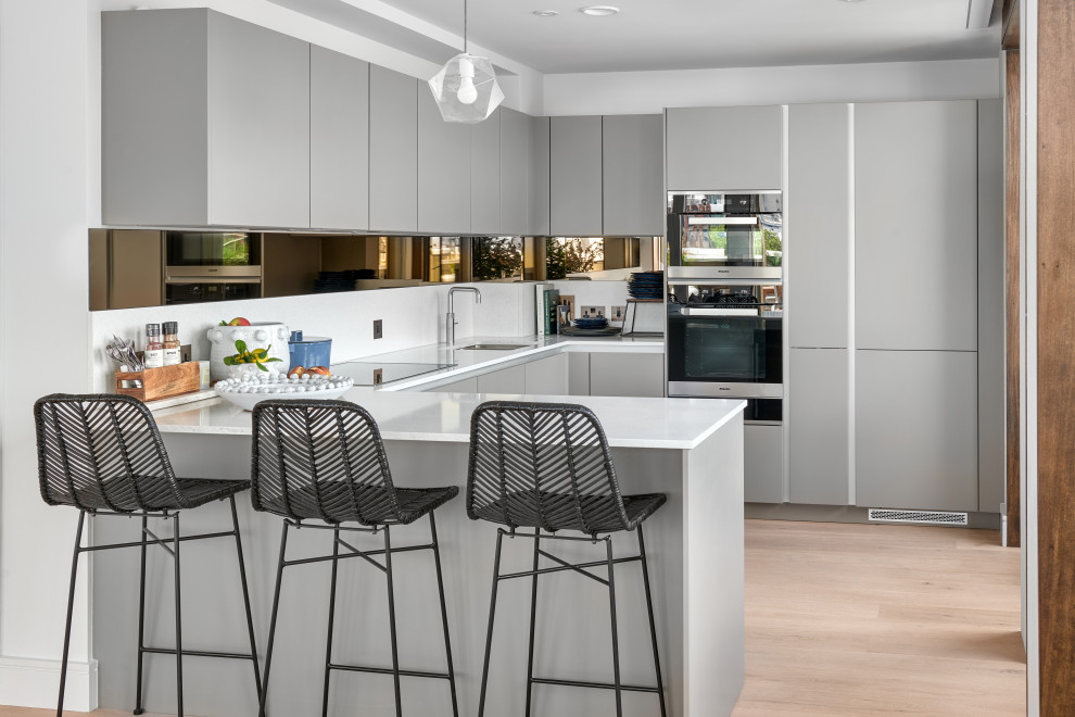 Inspiration for a small contemporary l-shaped open plan kitchen in Hampshire with a built-in sink, flat-panel cabinets, grey cabinets, granite worktops, white splashback, ceramic splashback, integrated appliances, light hardwood flooring, no island, brown floors and white worktops.