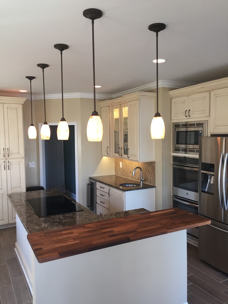 Large transitional l-shaped porcelain tile and brown floor open concept kitchen photo in Other with an undermount sink, beige backsplash, stainless steel appliances, an island, raised-panel cabinets, distressed cabinets, marble countertops, ceramic backsplash and brown countertops
