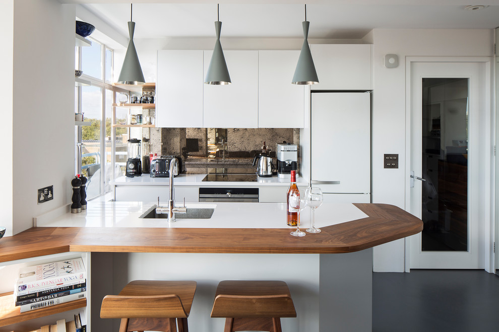 Modern inredning av ett litet linjärt kök med öppen planlösning, med en undermonterad diskho, släta luckor, vita skåp, stänkskydd med metallisk yta, spegel som stänkskydd, rostfria vitvaror, linoleumgolv, en halv köksö och grått golv