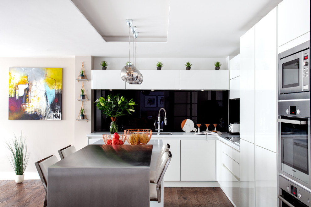 Inspiration for a contemporary l-shaped kitchen in London with a submerged sink, flat-panel cabinets, white cabinets, black splashback, stainless steel appliances, dark hardwood flooring, an island, brown floors and white worktops.