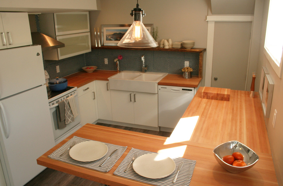 Photo of a small modern l-shaped kitchen/diner in Vancouver with a belfast sink, glass-front cabinets, white cabinets, wood worktops, blue splashback, ceramic splashback, white appliances and a breakfast bar.