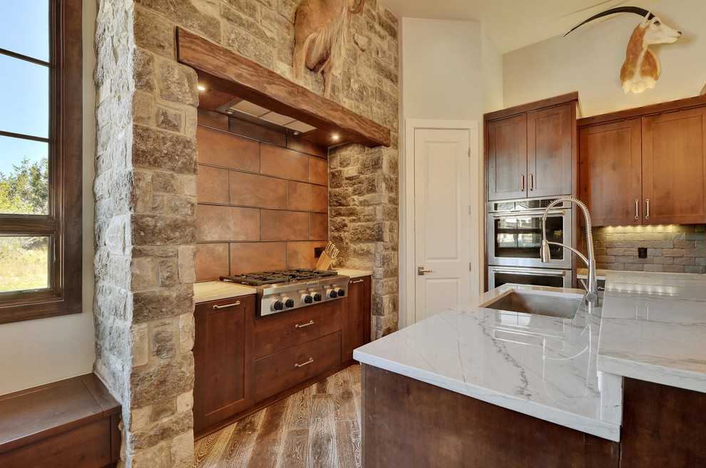 Photo of a large rustic u-shaped kitchen/diner in Austin with a submerged sink, shaker cabinets, medium wood cabinets, marble worktops, brown splashback, metal splashback, stainless steel appliances, medium hardwood flooring and an island.