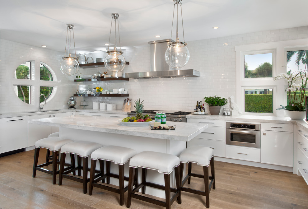 Küche in U-Form mit Unterbauwaschbecken, weißen Schränken, Küchenrückwand in Weiß, Rückwand aus Metrofliesen, braunem Holzboden und Kücheninsel in Sonstige
