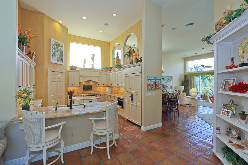 Bild på ett stort tropiskt kök, med en undermonterad diskho, beige skåp, granitbänkskiva, flerfärgad stänkskydd, klinkergolv i terrakotta, luckor med infälld panel, integrerade vitvaror, brunt golv och en köksö