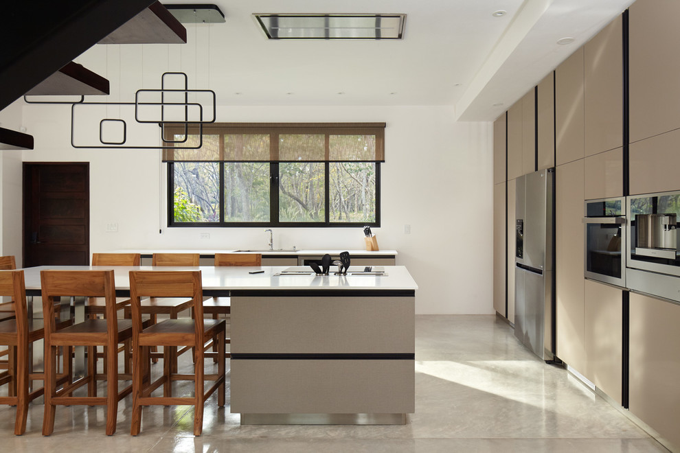 Cette photo montre une cuisine tendance avec un placard à porte plane, des portes de placard beiges, un électroménager en acier inoxydable, îlot, un sol gris et un plan de travail blanc.
