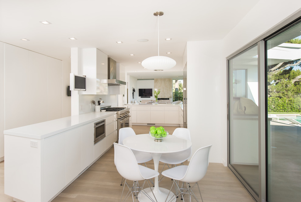 Immagine di una cucina minimal con ante lisce, ante bianche, elettrodomestici in acciaio inossidabile, parquet chiaro e pavimento beige
