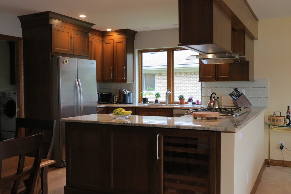 This is an example of a medium sized classic u-shaped open plan kitchen in Detroit with a submerged sink, flat-panel cabinets, medium wood cabinets, granite worktops, white splashback, glass tiled splashback, stainless steel appliances, medium hardwood flooring, a breakfast bar and brown floors.