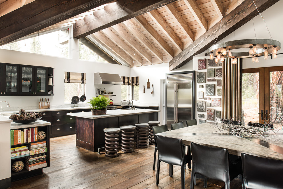 Eat-in kitchen - large industrial l-shaped medium tone wood floor eat-in kitchen idea in Sacramento with glass-front cabinets, black cabinets, stainless steel appliances, an island, an undermount sink, quartz countertops and white backsplash