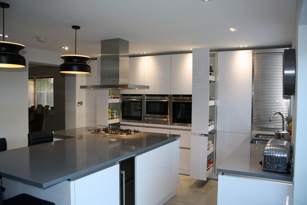 Bild på ett stort funkis kök, med en undermonterad diskho, släta luckor, vita skåp, bänkskiva i kvarts, grått stänkskydd, rostfria vitvaror, marmorgolv och en köksö