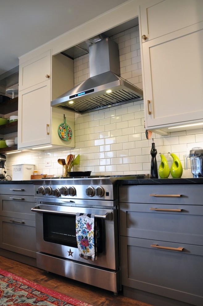 Bild på ett mellanstort retro svart svart kök, med en undermonterad diskho, skåp i shakerstil, grå skåp, vitt stänkskydd, stänkskydd i tunnelbanekakel, rostfria vitvaror, mörkt trägolv, en halv köksö, brunt golv och bänkskiva i täljsten