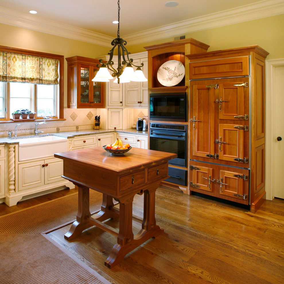 Foto på ett lantligt kök, med en rustik diskho, vita skåp, granitbänkskiva, vitt stänkskydd, stänkskydd i stenkakel, integrerade vitvaror, mellanmörkt trägolv och luckor med upphöjd panel