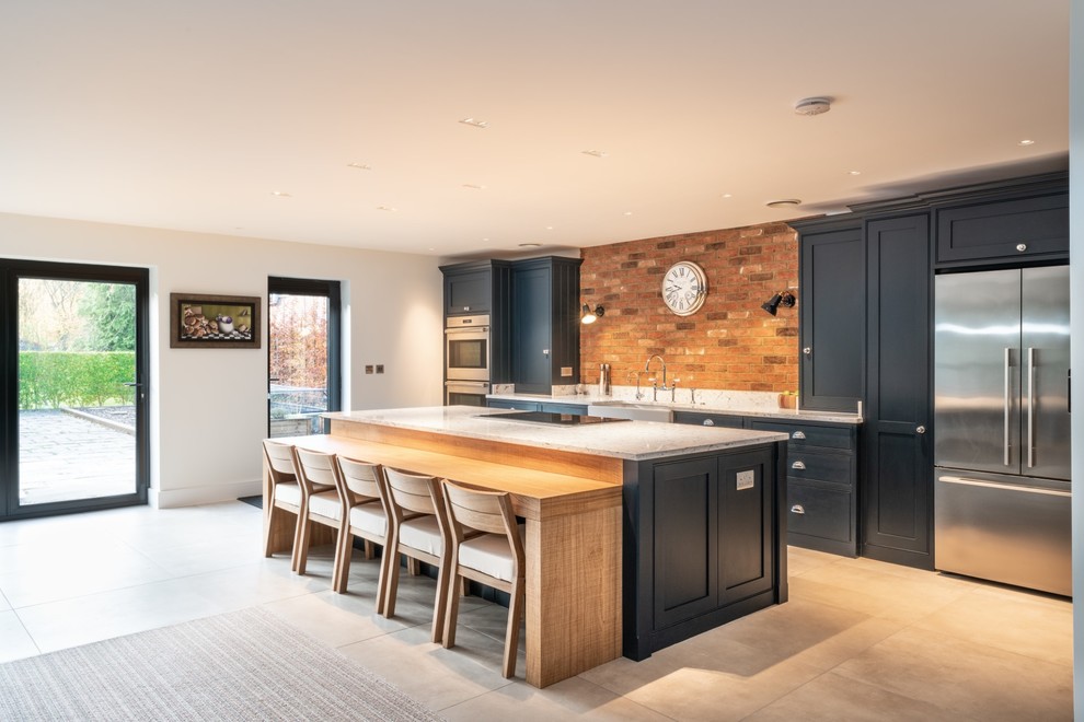 Photo of an expansive contemporary single-wall open plan kitchen in Essex with a belfast sink, beaded cabinets, blue cabinets, quartz worktops, multi-coloured splashback, brick splashback, stainless steel appliances, terracotta flooring, an island, beige floors and white worktops.