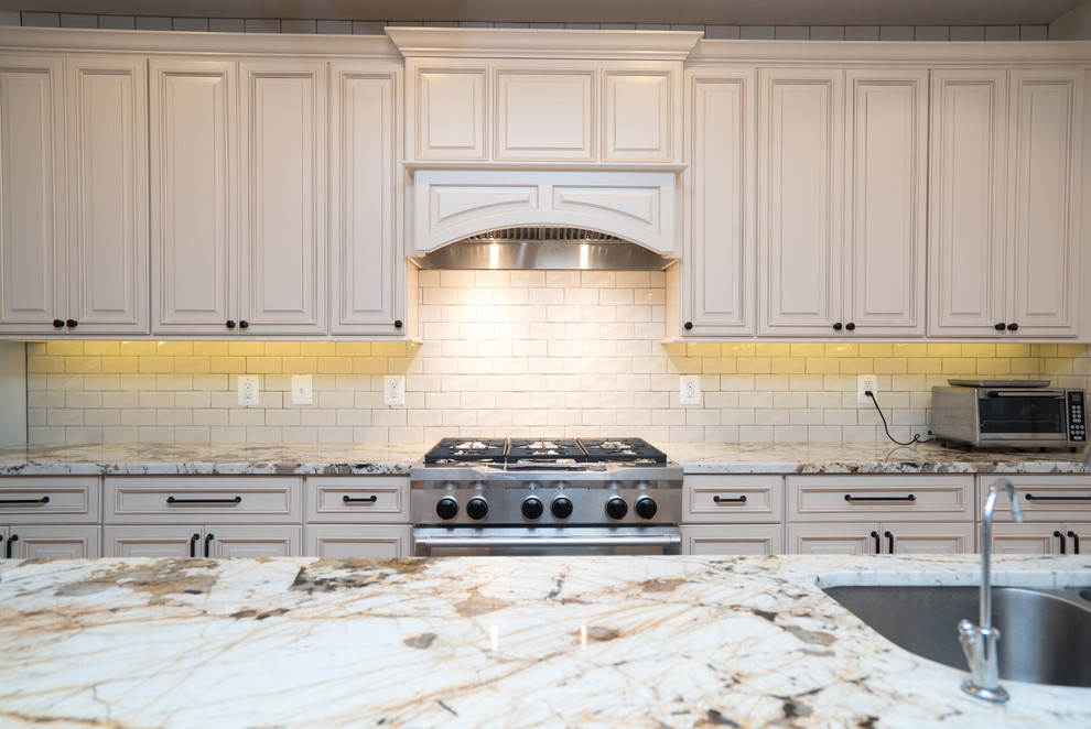 Exempel på ett stort klassiskt kök, med luckor med upphöjd panel, vita skåp, granitbänkskiva, vitt stänkskydd, stänkskydd i keramik, rostfria vitvaror och en köksö