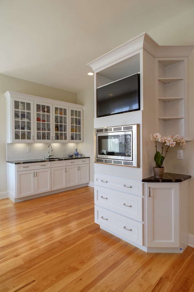 Cette photo montre une cuisine parallèle nature avec des portes de placard blanches, une crédence blanche, un électroménager en acier inoxydable et îlot.