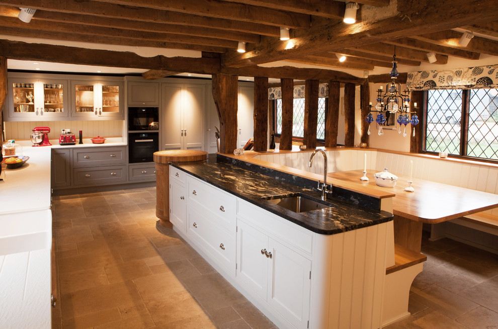 Foto di una cucina country con lavello sottopiano, ante in stile shaker, ante bianche, paraspruzzi bianco, elettrodomestici neri e pavimento beige