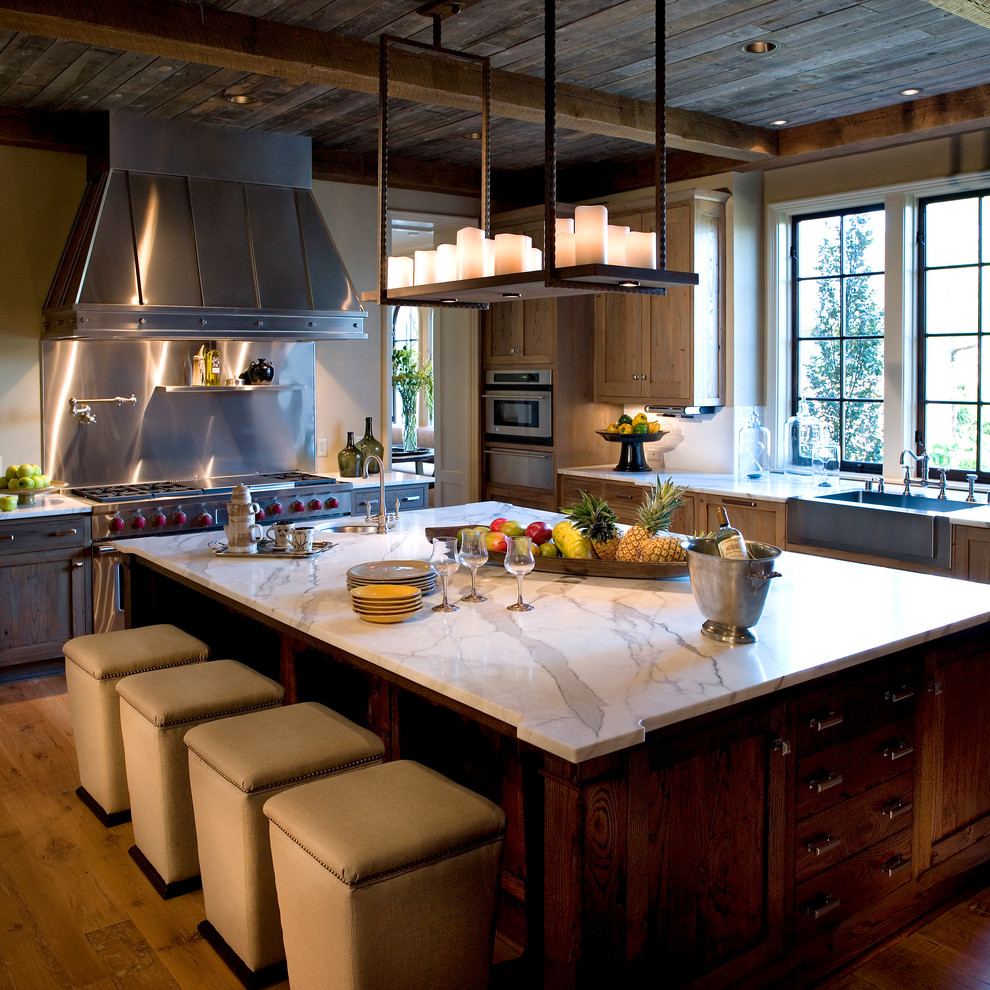 Klassisk inredning av ett stort u-kök, med en rustik diskho, luckor med infälld panel, skåp i mörkt trä, marmorbänkskiva, beige stänkskydd, rostfria vitvaror, mellanmörkt trägolv och en köksö
