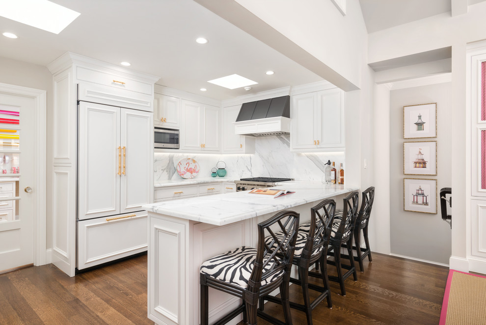 Inredning av ett klassiskt mellanstort vit vitt kök, med en undermonterad diskho, luckor med infälld panel, vita skåp, marmorbänkskiva, gult stänkskydd, stänkskydd i marmor, rostfria vitvaror, mellanmörkt trägolv, en halv köksö och brunt golv
