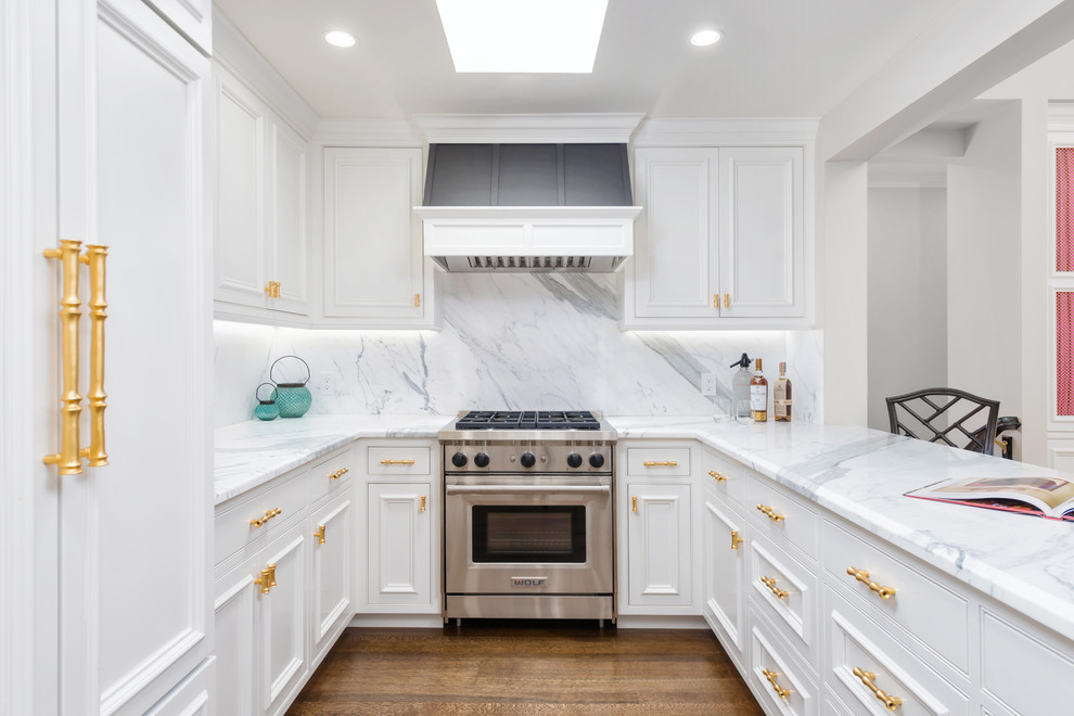 Klassisk inredning av ett mellanstort vit vitt kök, med en undermonterad diskho, luckor med infälld panel, vita skåp, marmorbänkskiva, gult stänkskydd, stänkskydd i marmor, rostfria vitvaror, mellanmörkt trägolv, en halv köksö och brunt golv
