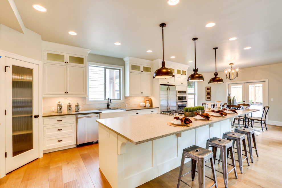 Zweizeilige Klassische Wohnküche mit Landhausspüle, Schrankfronten mit vertiefter Füllung, weißen Schränken, Küchenrückwand in Beige, Küchengeräten aus Edelstahl, braunem Holzboden und Kücheninsel in Portland