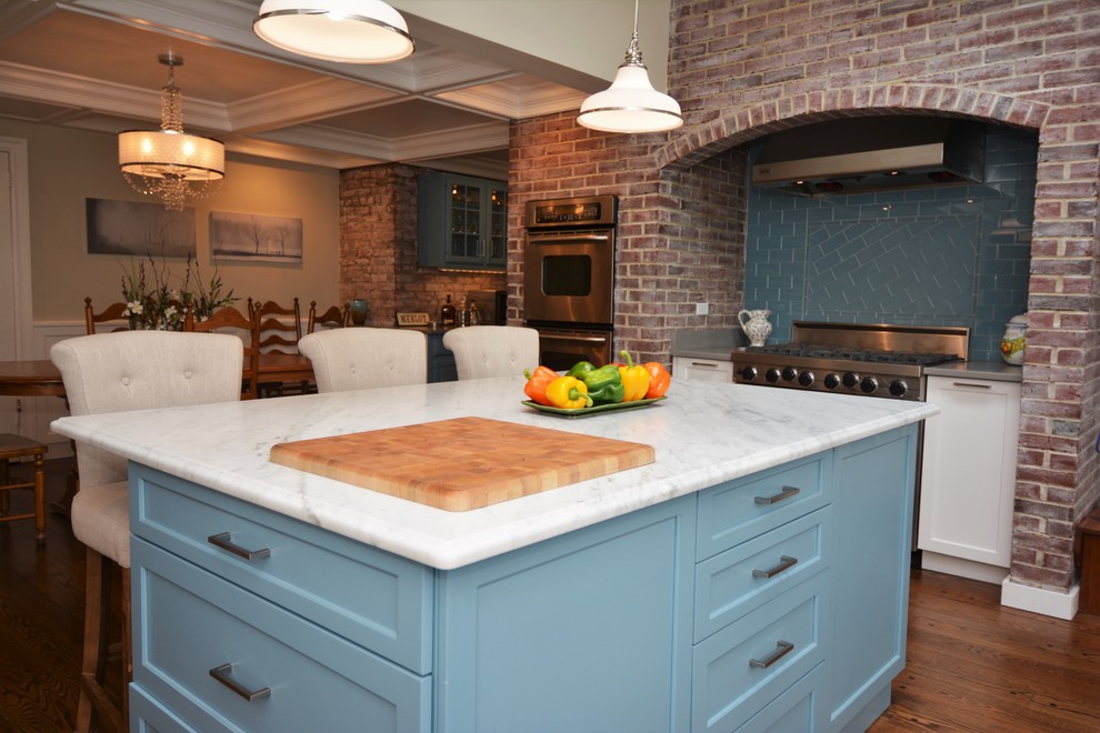 Klassisk inredning av ett stort kök, med en undermonterad diskho, luckor med infälld panel, blå skåp, marmorbänkskiva, blått stänkskydd, stänkskydd i glaskakel, rostfria vitvaror, mellanmörkt trägolv och en köksö