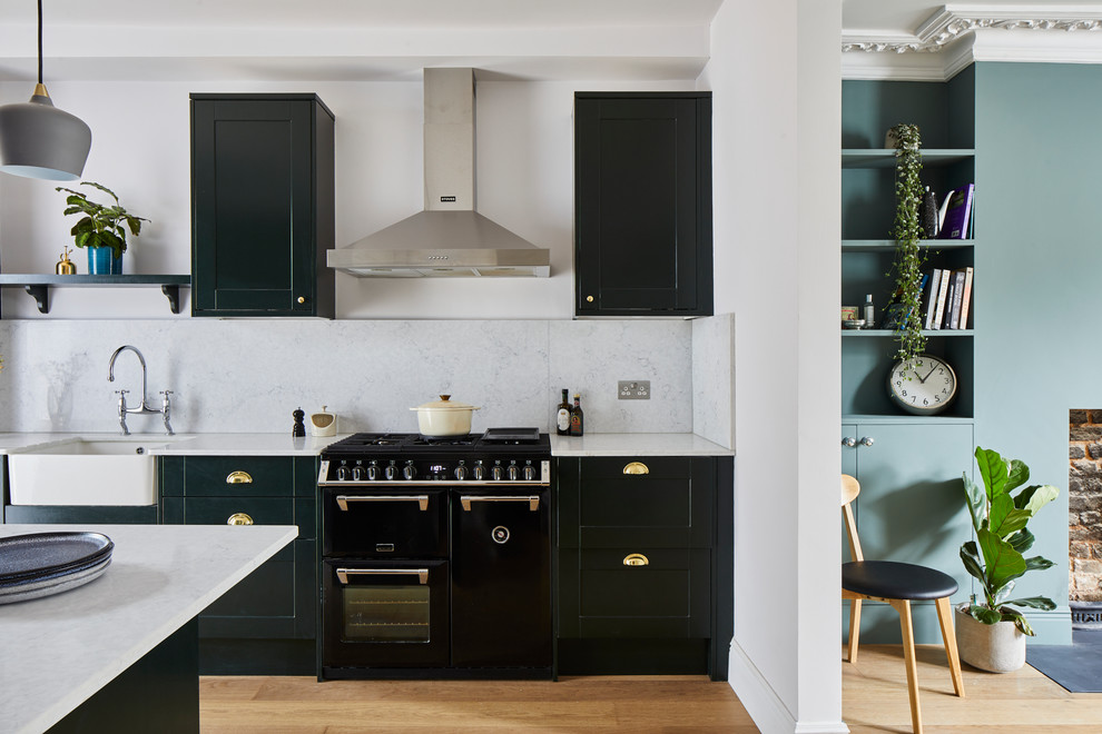 Inspiration for a transitional galley medium tone wood floor and brown floor kitchen remodel in London with a farmhouse sink, shaker cabinets, black cabinets, white backsplash, black appliances, an island and white countertops
