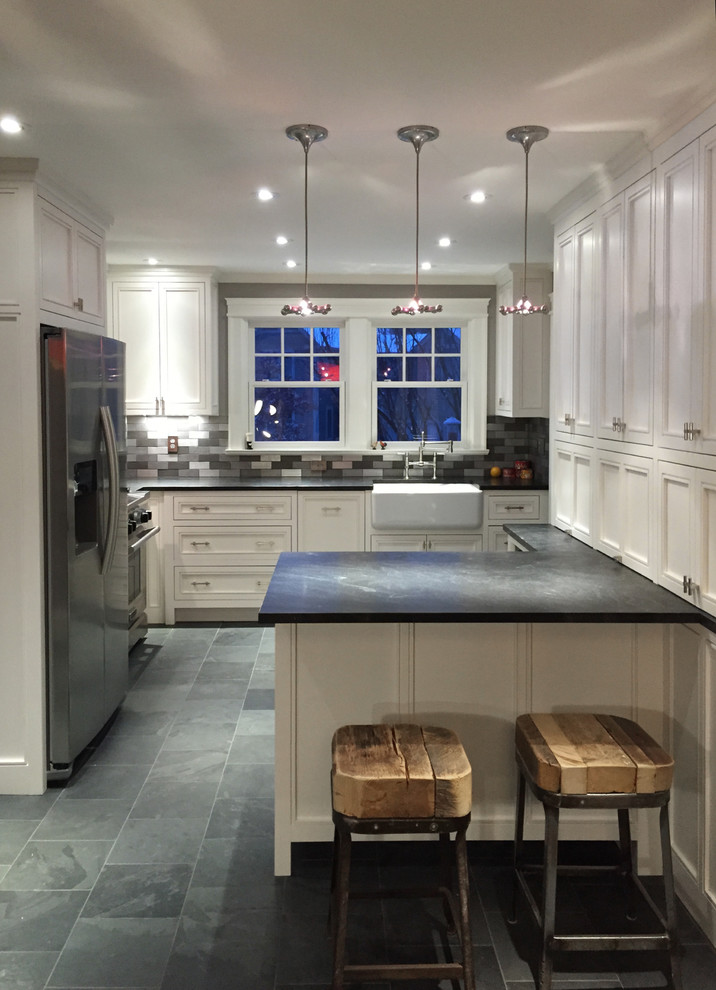 Inredning av ett klassiskt mellanstort l-kök, med en rustik diskho, luckor med infälld panel, vita skåp, granitbänkskiva, stänkskydd med metallisk yta, stänkskydd i metallkakel, rostfria vitvaror, skiffergolv och en halv köksö