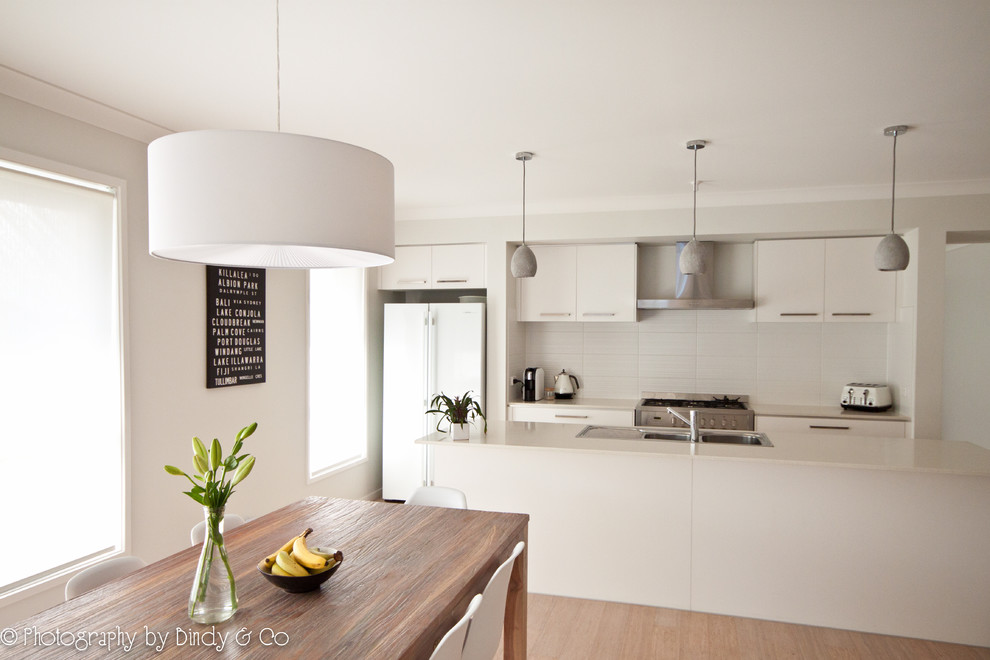 Photo of a large modern single-wall open plan kitchen in Wollongong with a double-bowl sink, flat-panel cabinets, white cabinets, engineered stone countertops, white splashback, ceramic splashback, stainless steel appliances, bamboo flooring and an island.