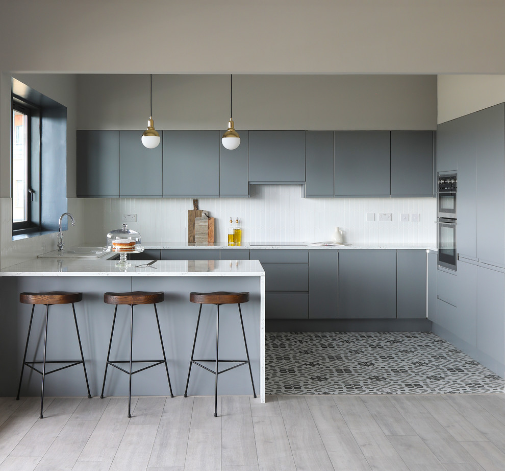 Inspiration for a contemporary u-shaped kitchen in Dublin with flat-panel cabinets, grey cabinets, laminate countertops, white splashback, ceramic splashback, integrated appliances, cement flooring, grey floors, white worktops and a breakfast bar.