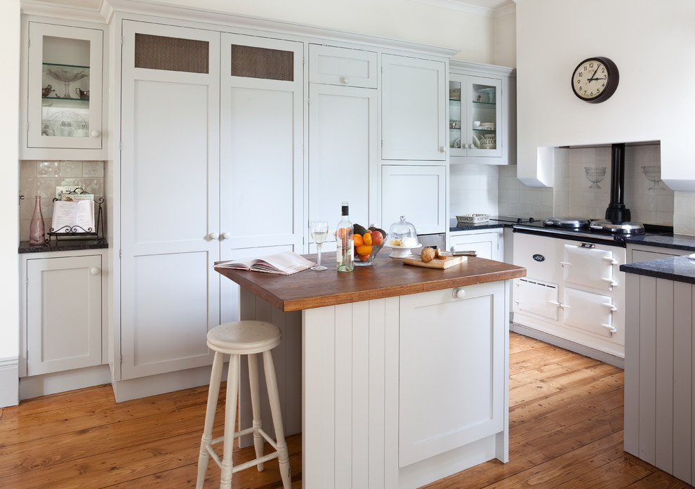 Klassische Küche in U-Form mit Schrankfronten im Shaker-Stil, blauen Schränken, Arbeitsplatte aus Holz, Küchenrückwand in Weiß, weißen Elektrogeräten, braunem Holzboden und Kücheninsel in London