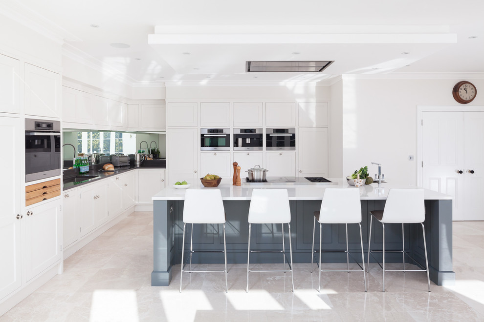 Kitchen - transitional l-shaped travertine floor kitchen idea in Gloucestershire with shaker cabinets, white cabinets, stainless steel appliances and an island