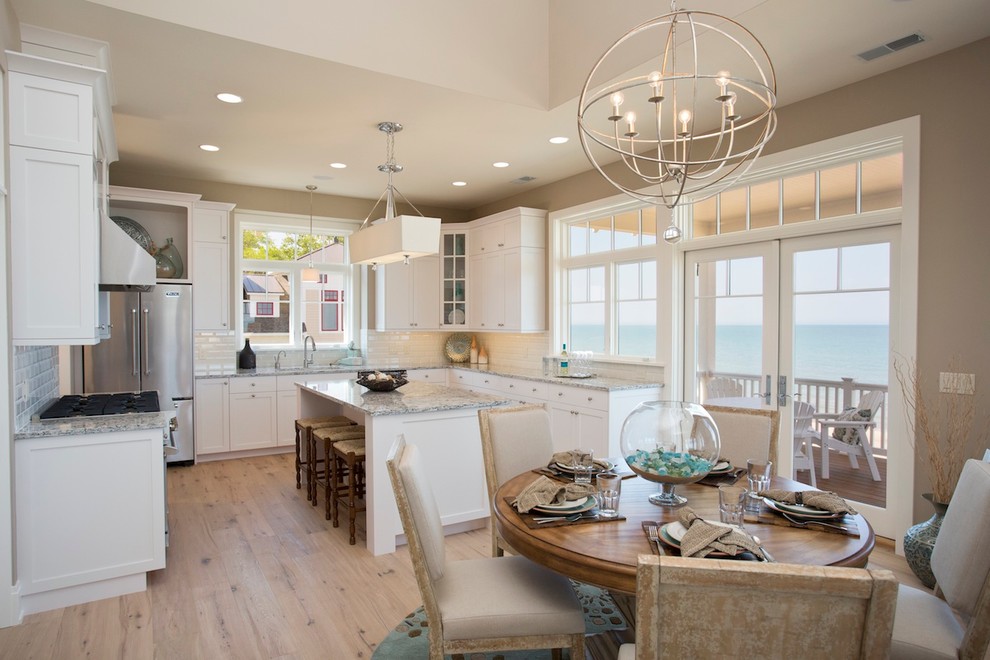 This is an example of a large coastal u-shaped kitchen in Grand Rapids with a double-bowl sink, recessed-panel cabinets, white cabinets, granite worktops, stainless steel appliances, light hardwood flooring and an island.