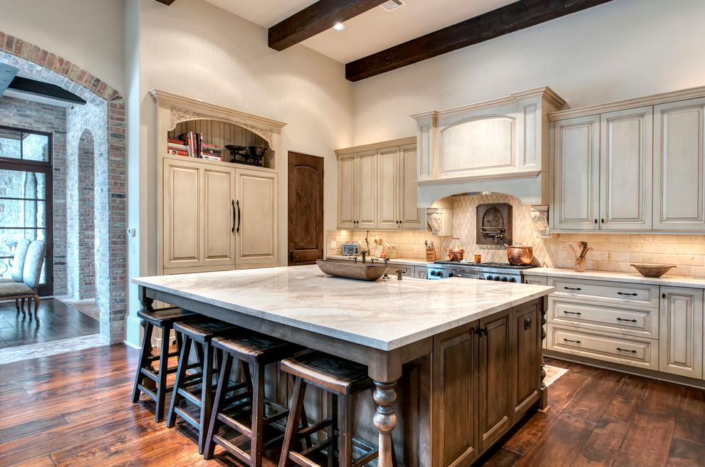 Open concept kitchen - huge mediterranean u-shaped dark wood floor and brown floor open concept kitchen idea in Houston with a farmhouse sink, raised-panel cabinets, distressed cabinets, marble countertops, beige backsplash, stone tile backsplash, paneled appliances and an island