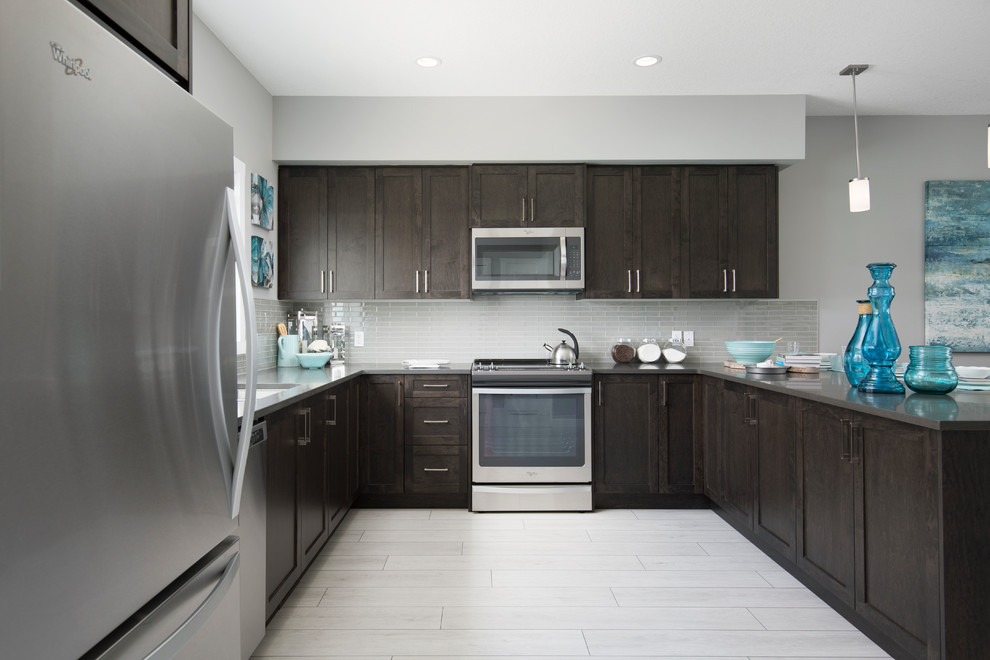 Modern inredning av ett mellanstort kök, med en undermonterad diskho, skåp i shakerstil, skåp i mörkt trä, granitbänkskiva, grått stänkskydd, stänkskydd i glaskakel, rostfria vitvaror, laminatgolv, en halv köksö och grått golv
