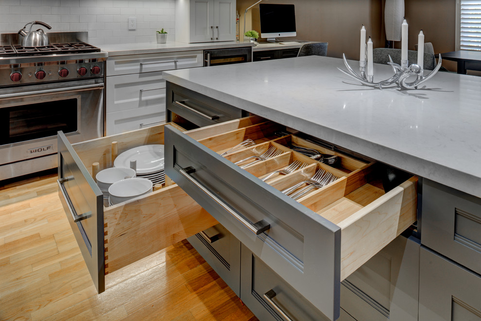 Example of a mid-sized transitional l-shaped light wood floor kitchen pantry design in San Francisco with an undermount sink, recessed-panel cabinets, white cabinets, quartz countertops, white backsplash, ceramic backsplash, stainless steel appliances and an island