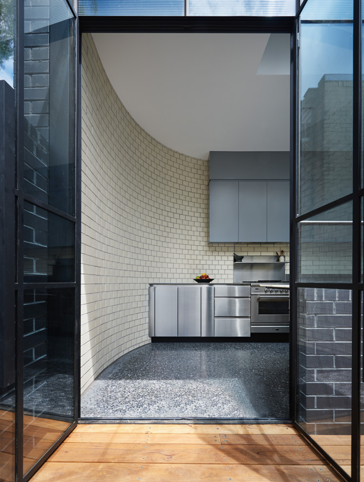 Idéer för att renovera ett mellanstort funkis kök, med en dubbel diskho, släta luckor, skåp i rostfritt stål, bänkskiva i rostfritt stål, vitt stänkskydd, stänkskydd i tegel, rostfria vitvaror, betonggolv och svart golv