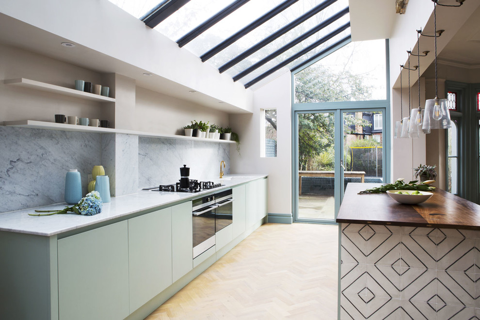 Photo of a contemporary single-wall kitchen in London with flat-panel cabinets, green cabinets, wood worktops, grey splashback, black appliances, light hardwood flooring, an island and yellow floors.