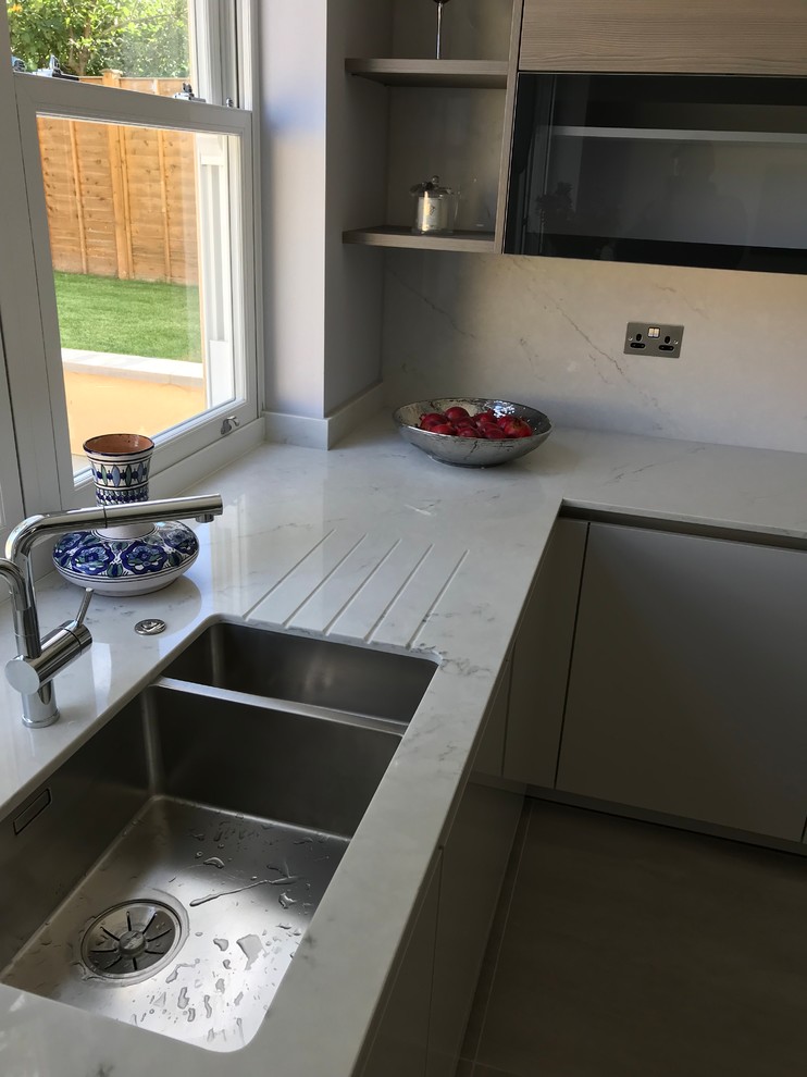 Photo of a medium sized contemporary grey and cream l-shaped kitchen/diner in Buckinghamshire with flat-panel cabinets, beige cabinets, quartz worktops, beige splashback, an island and beige worktops.