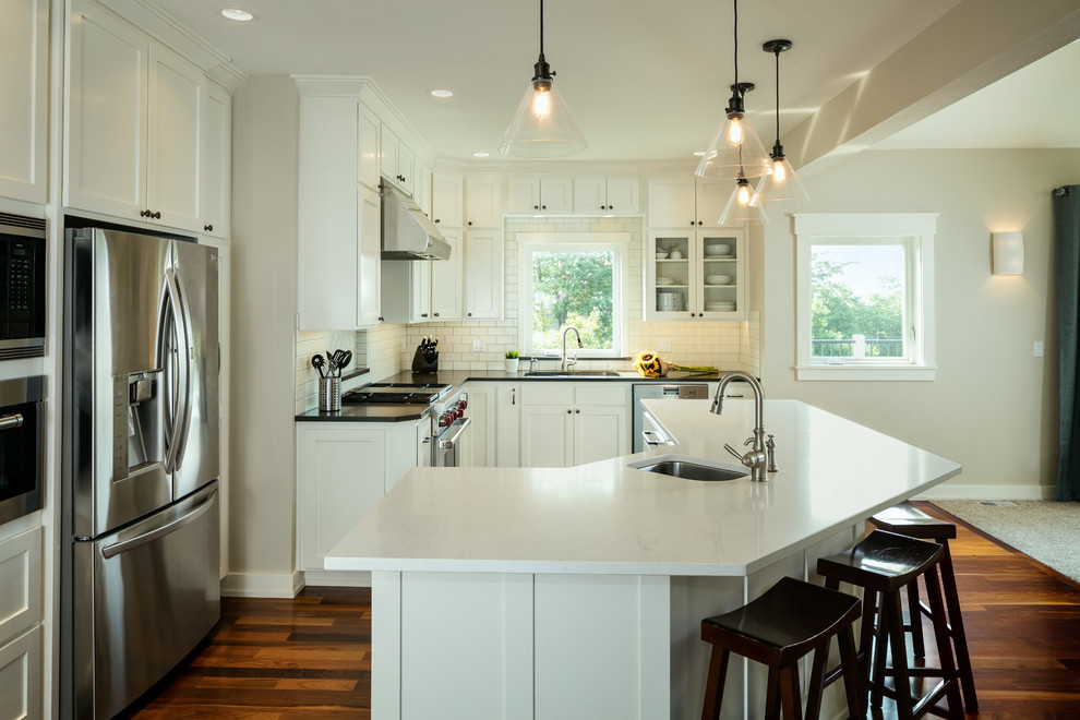 Example of a mid-sized classic u-shaped dark wood floor eat-in kitchen design in Other with an undermount sink, shaker cabinets, white cabinets, quartzite countertops, white backsplash, subway tile backsplash, stainless steel appliances, an island and black countertops