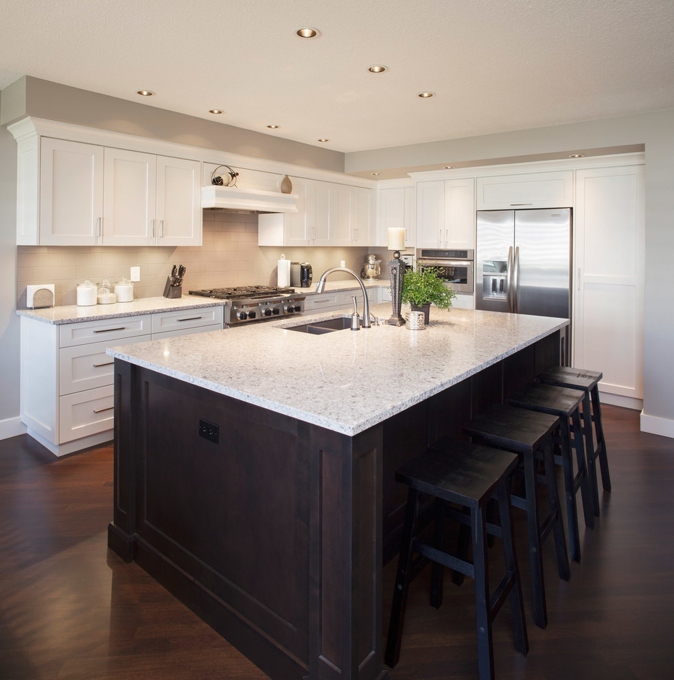 Mittelgroße Klassische Küche in L-Form mit Doppelwaschbecken, Schrankfronten im Shaker-Stil, weißen Schränken, Granit-Arbeitsplatte, Küchengeräten aus Edelstahl, dunklem Holzboden, Kücheninsel und braunem Boden in Calgary