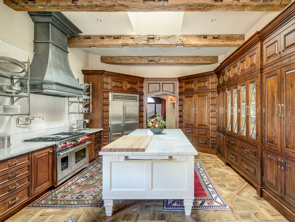 Immagine di una cucina mediterranea chiusa con ante con bugna sagomata, ante in legno bruno, top in marmo, paraspruzzi bianco, paraspruzzi in lastra di pietra, elettrodomestici da incasso e parquet chiaro