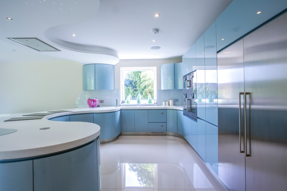 Photo of an expansive modern l-shaped open plan kitchen in London with an integrated sink, flat-panel cabinets, blue cabinets, composite countertops, grey splashback, glass sheet splashback, stainless steel appliances, porcelain flooring and a breakfast bar.