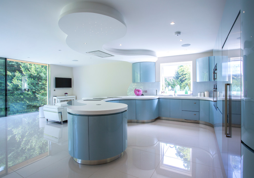 Design ideas for an expansive modern l-shaped open plan kitchen in London with an integrated sink, flat-panel cabinets, blue cabinets, composite countertops, grey splashback, glass sheet splashback, stainless steel appliances, porcelain flooring and a breakfast bar.