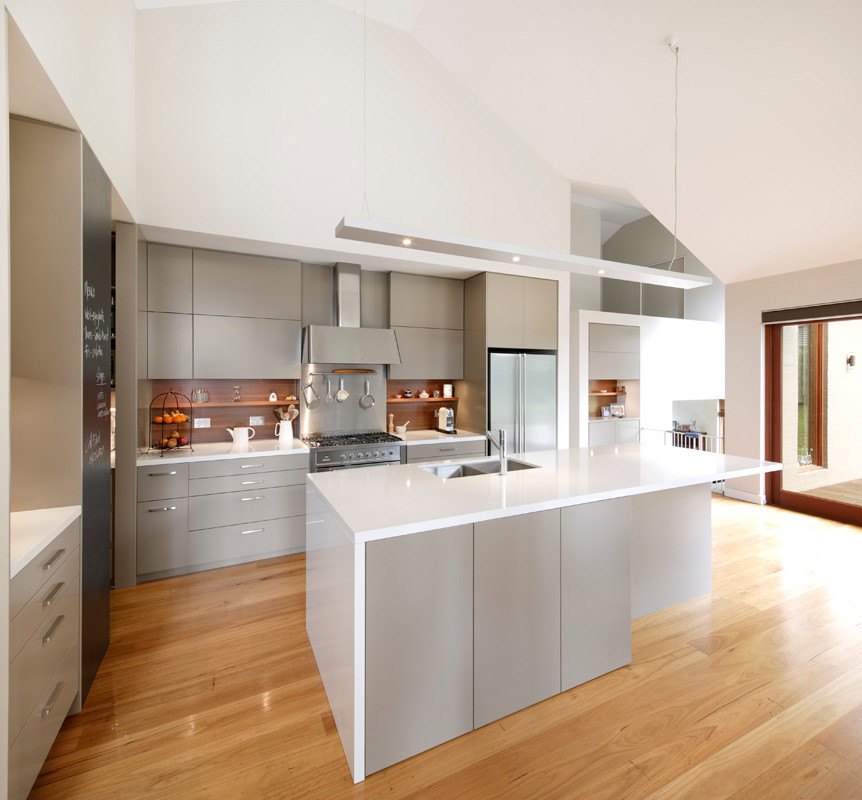 This is an example of a medium sized contemporary galley kitchen/diner in Sydney with a submerged sink, flat-panel cabinets, beige cabinets, engineered stone countertops, brown splashback, wood splashback, stainless steel appliances, medium hardwood flooring and an island.