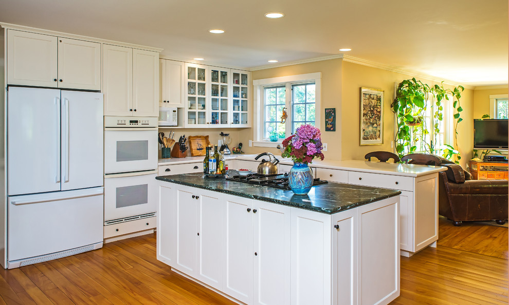 This is an example of a kitchen in Boston with beaded cabinets, white cabinets, marble worktops, white appliances, medium hardwood flooring, an island, brown floors and green worktops.