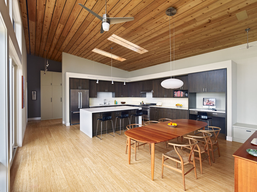 Moderne Wohnküche in L-Form mit flächenbündigen Schrankfronten, dunklen Holzschränken, Küchenrückwand in Weiß und Küchengeräten aus Edelstahl in Orange County