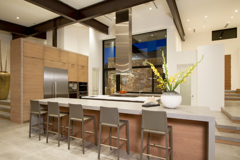 Immagine di una cucina minimal con lavello sottopiano, ante lisce, ante in legno chiaro, paraspruzzi a finestra, elettrodomestici in acciaio inossidabile, 2 o più isole e pavimento beige