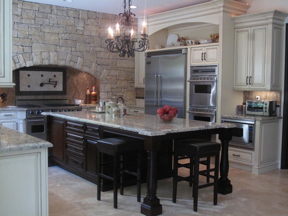 Large tuscan u-shaped travertine floor eat-in kitchen photo in Los Angeles with recessed-panel cabinets, granite countertops, multicolored backsplash, stone tile backsplash, stainless steel appliances, an island and a farmhouse sink