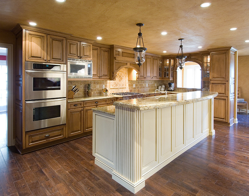 Idées déco pour une grande cuisine américaine campagne en L et bois vieilli avec un évier encastré, un placard avec porte à panneau surélevé, un plan de travail en granite, une crédence beige, une crédence en céramique, un électroménager en acier inoxydable, parquet foncé, îlot et un sol marron.