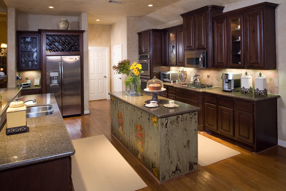 Example of a large tuscan galley medium tone wood floor open concept kitchen design in Austin with granite countertops, stone tile backsplash, paneled appliances, a double-bowl sink, beige backsplash, two islands, raised-panel cabinets and dark wood cabinets