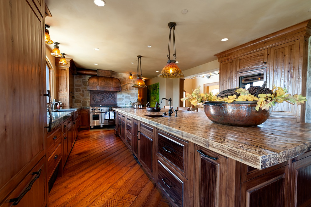 Large u-shaped kitchen/diner in San Diego with a belfast sink, raised-panel cabinets, light wood cabinets, granite worktops, beige splashback, limestone splashback, integrated appliances, medium hardwood flooring, an island and brown floors.